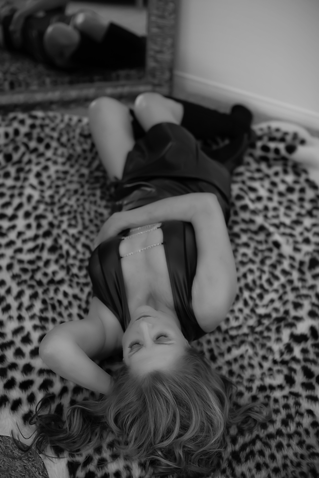 Black and White photo of a woman in her sixties wearing lingerie on a leopard rug for a boudoir session by Kellie Foster