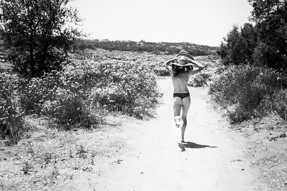 Black and White photo of a woman running down a trail in a hat and underwear. 