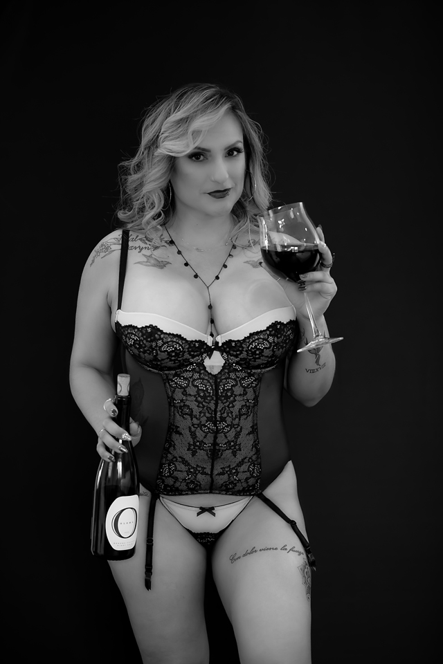 black and white photo of a woman in lingerie holding a wine glass and bottle of wine